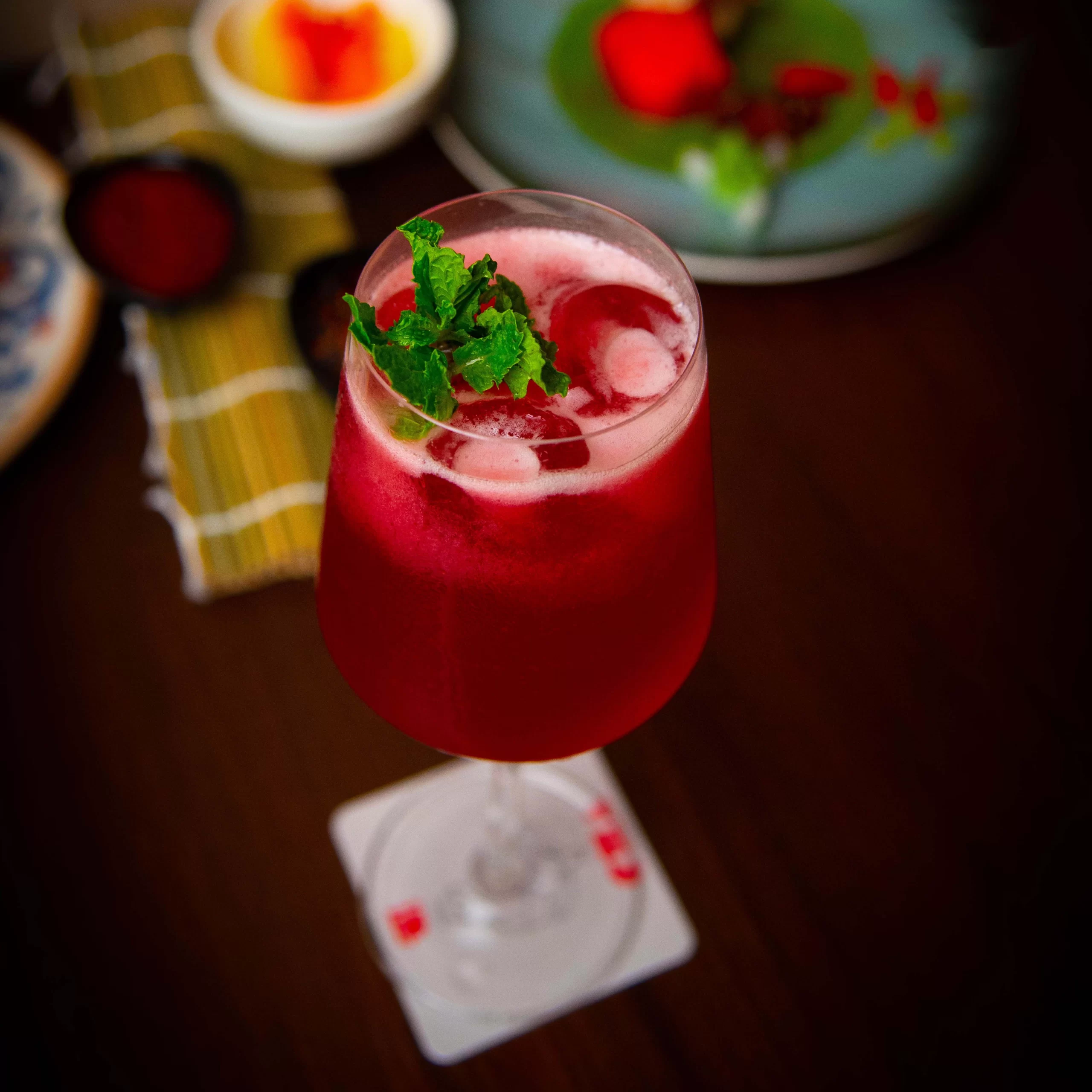 Photography Portfolio Vibrant red signature cocktail with fresh mint garnish and ice in elegant glass with blurred restaurant background - Content Crest Media beverage and cocktail photography portfolio Ahmedabad Gujarat