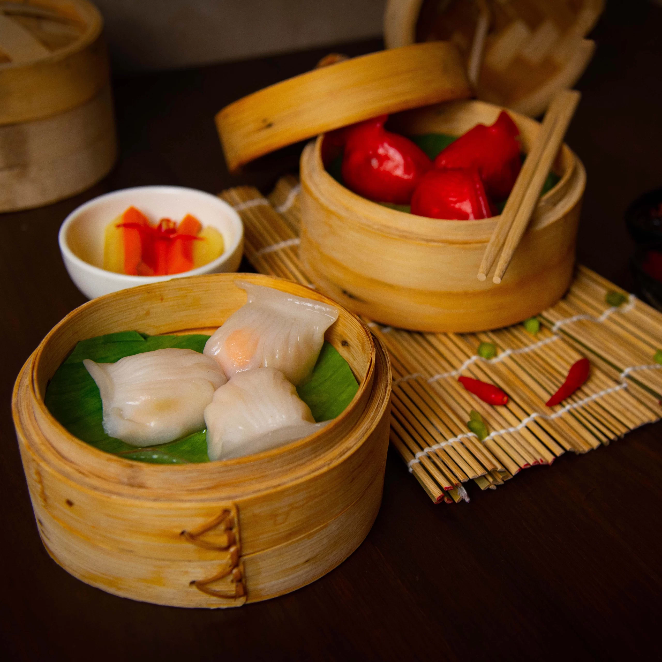 Photography Portfolio Traditional bamboo steamer baskets with crystal shrimp dumplings and red-wrapped dim sum with pickled vegetables - Content Crest Media Asian restaurant food photography portfolio Ahmedabad Gujarat