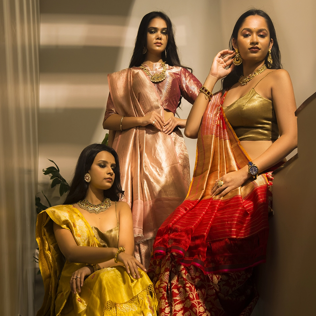 Photography Portfolio Contemporary ethnic fashion campaign with three models in golden yellow, peach and red silk sarees with traditional jewelry in architectural interior - Content Crest Media multi-model fashion photography portfolio Ahmedabad Gujarat